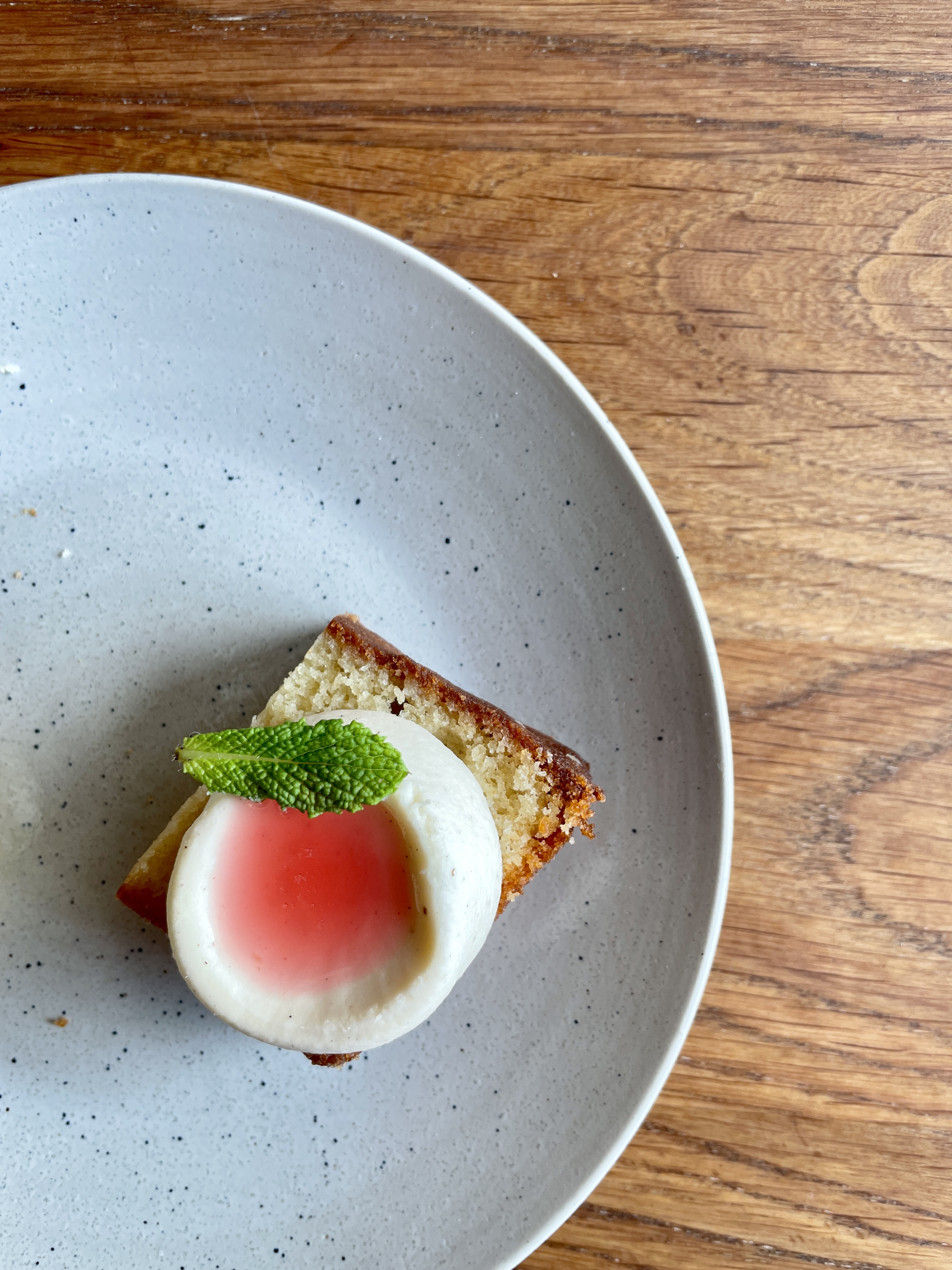 kage med creme, rabarberkompot og mynteblad står på en tallerken, som står på et træbord