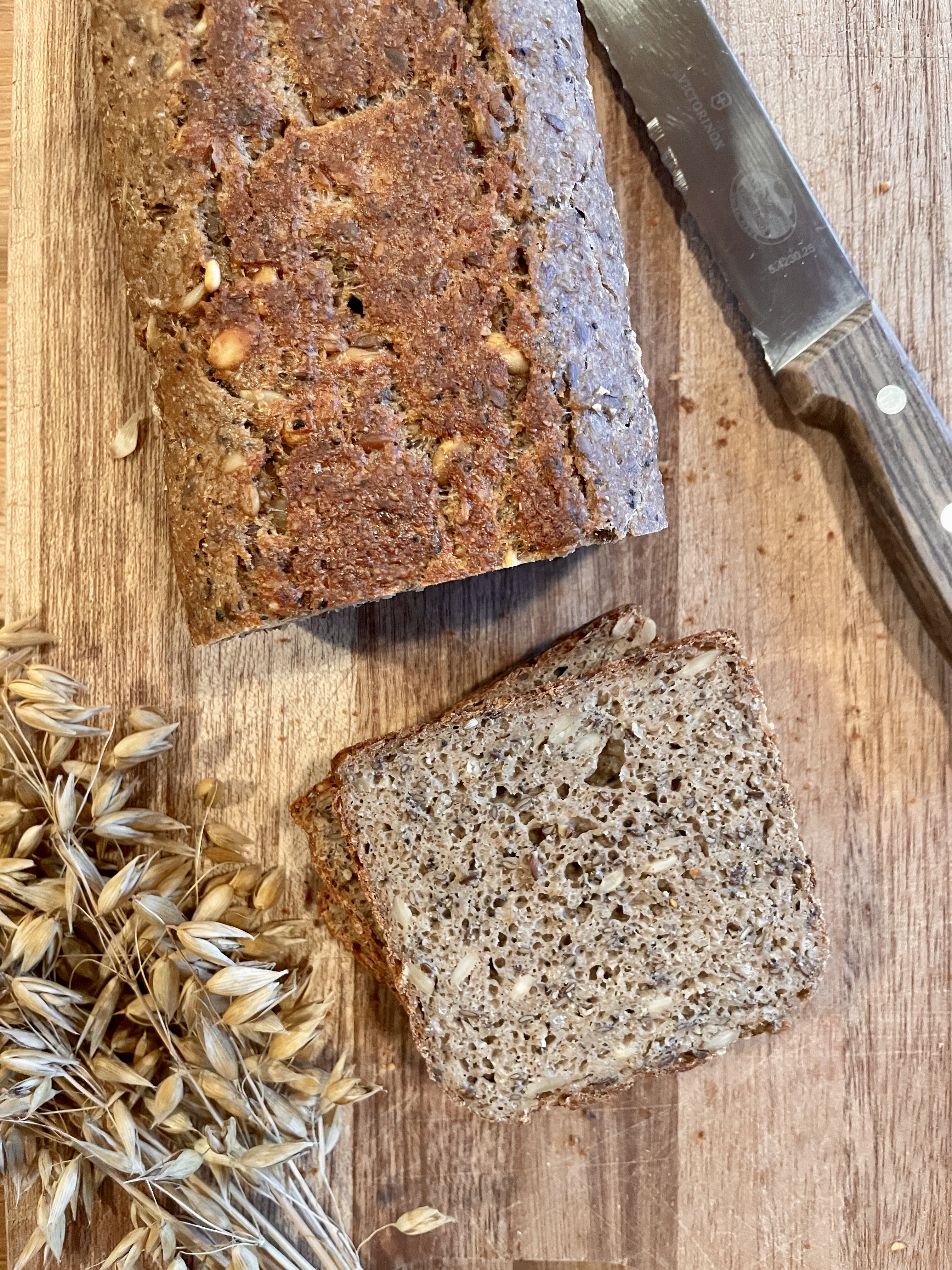 Brød, kornaks og brødkniv ligger på skærebræt i træ