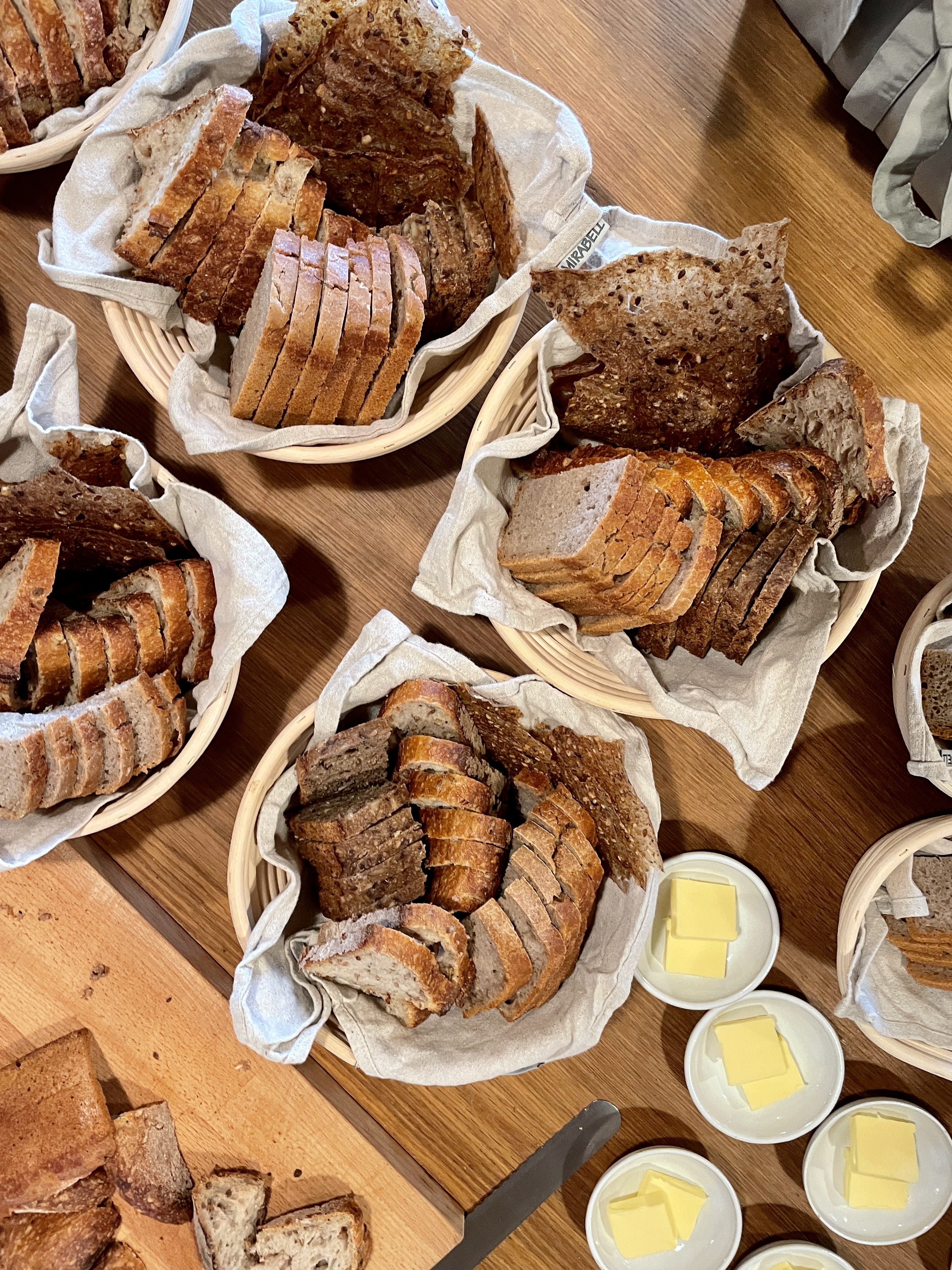 brødkurve med skåret brød og smørskåle med smør på træbord