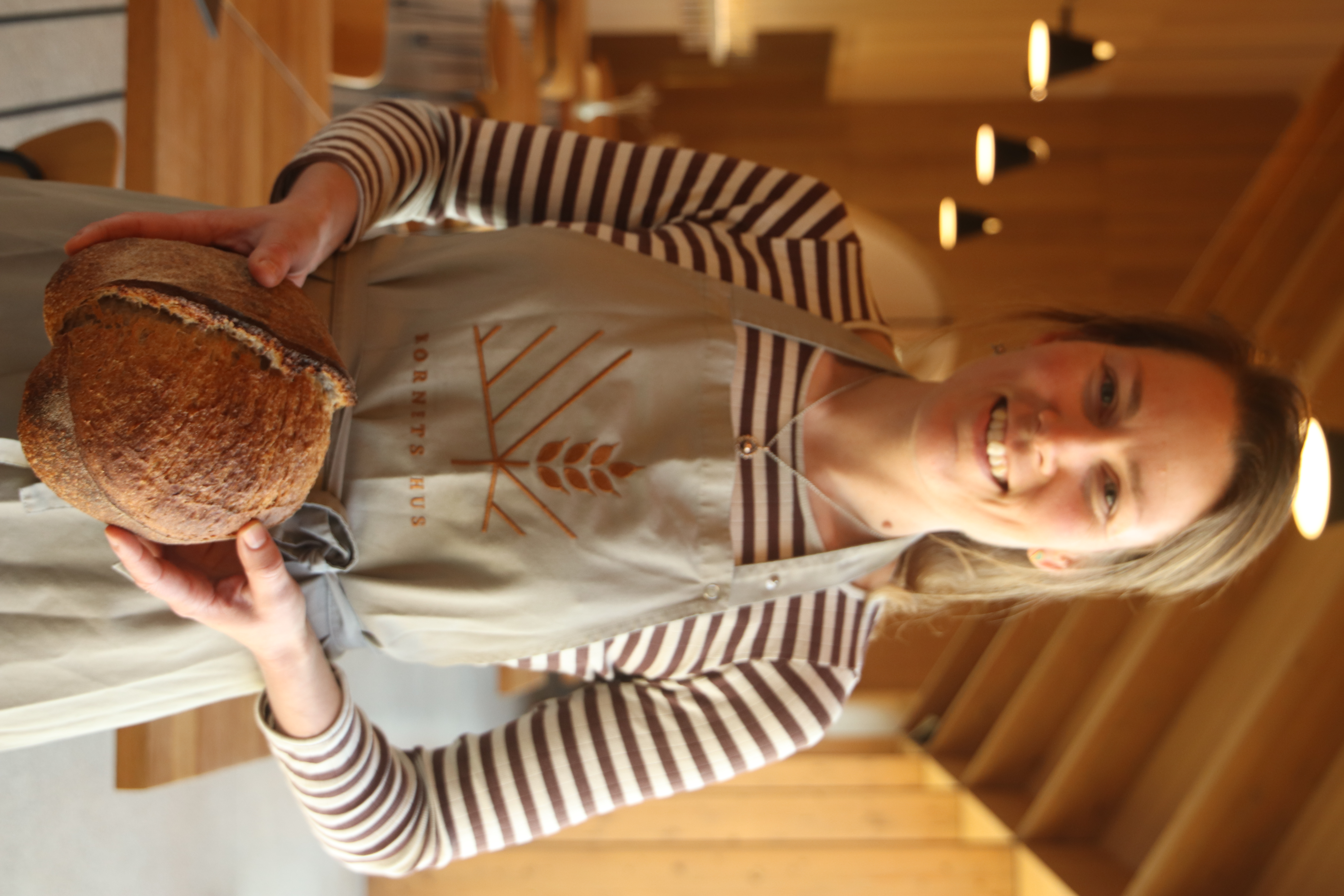 smilende kvinde med forklæde holder surdejsbrød i hænderne